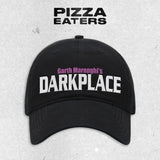 A black baseball cap with Garth Merenghi Text on the front in white and pink embroidered cotton. 